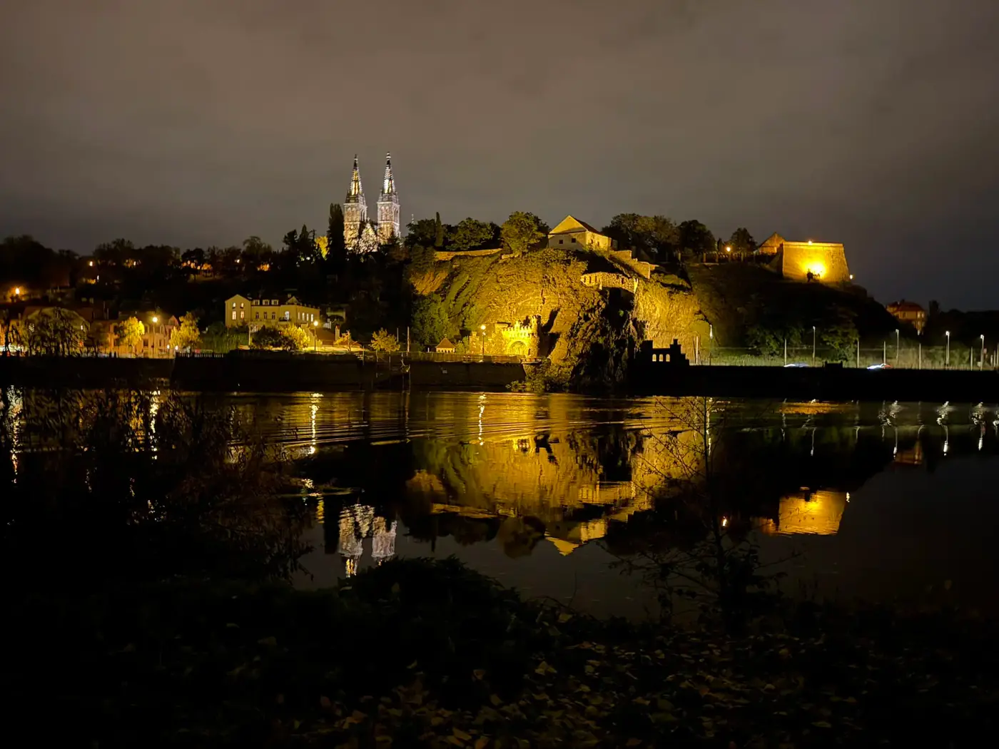 Vyšehrad basilica lit at dusk, reflected on the Vltava — the view from your dome